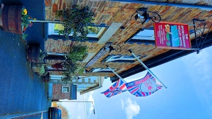 A street view of a building with a sign for 'The Sportsman's Valley Hotel' advertising food, wine, and accommodation. There are flags and a bicycle parked outside. - Sportsmans Valley Hotel (Liskeard)