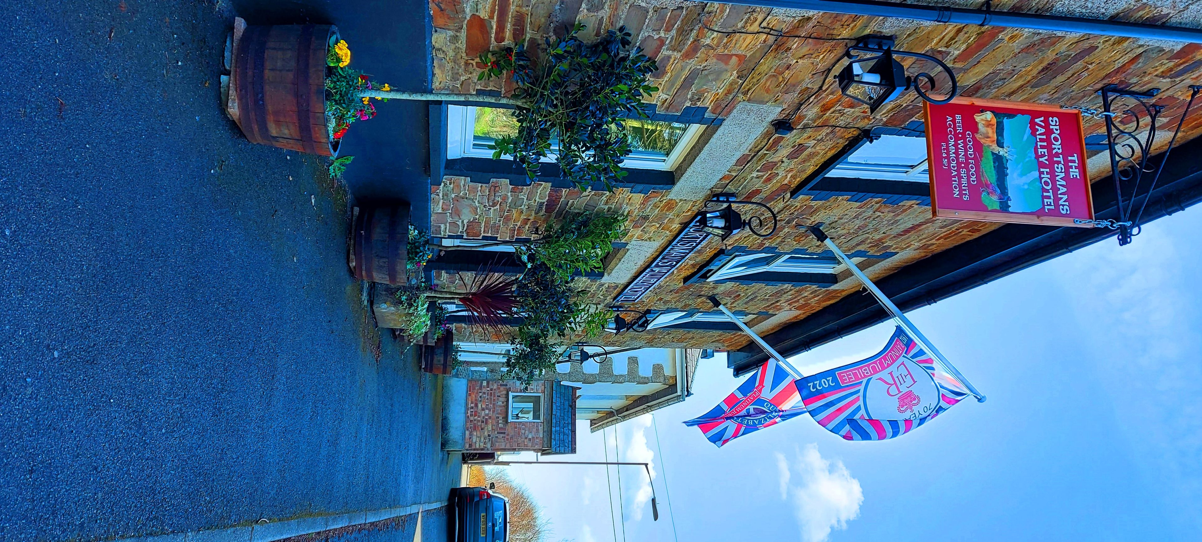 A street view of a building with a sign for 'The Sportsman's Valley Hotel' advertising food, wine, and accommodation. There are flags and a bicycle parked outside.