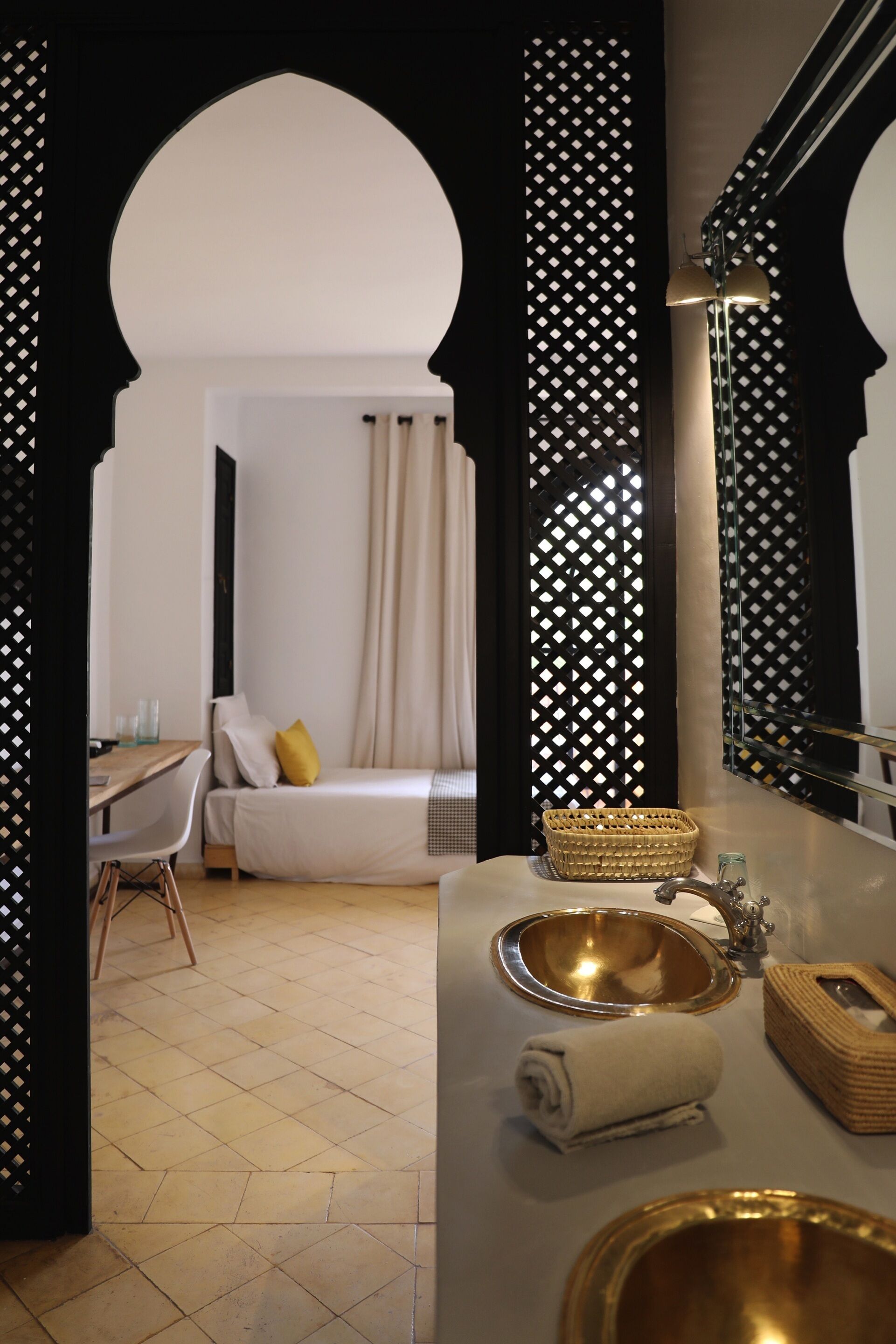 A hotel room with a bed, a desk, a bathroom with a sink and mirror, and a decorative wall with a geometric pattern.
