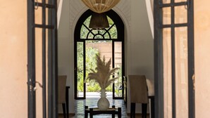 An arched doorway leading to a room with a large hanging light fixture, a potted plant, and a view of greenery outside. -  Villa Al Assala Palmeraie - Piscine chauffée (Marrakech)