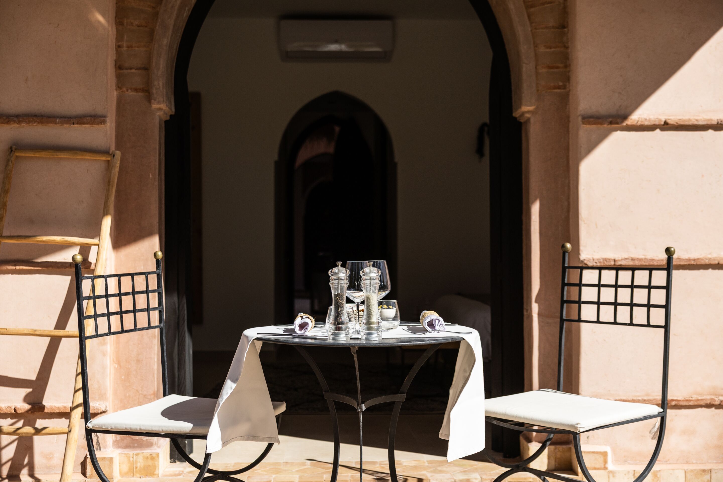 A table set with glasses and a salt shaker, two chairs, and an archway leading to a dark interior.