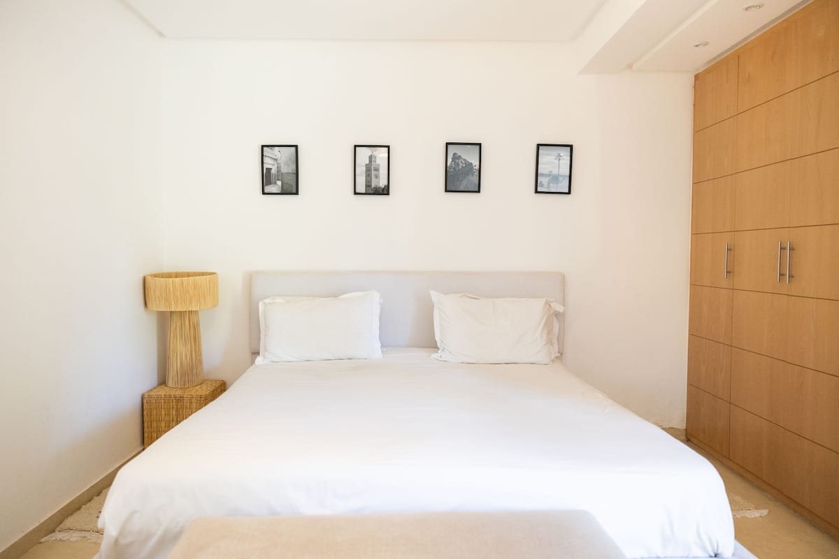 A bedroom with a bed, a nightstand, a lamp, a wardrobe, and four framed pictures on the wall.