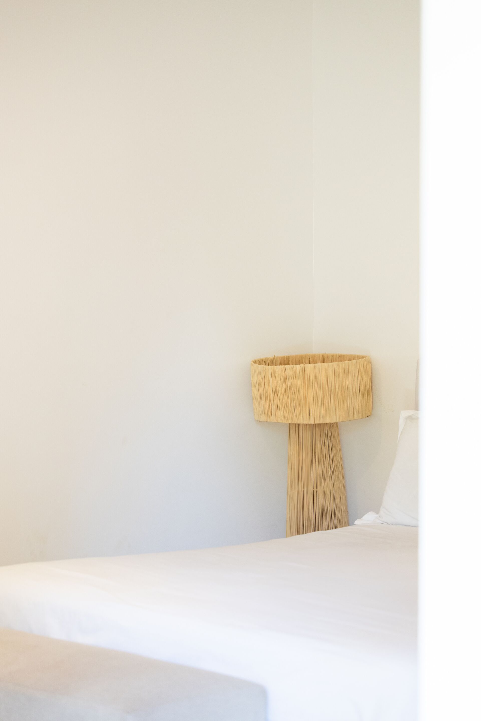 A bed with a white sheet, a wall-mounted lamp, and a white pillow.