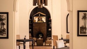 A hotel lobby with an arched doorway, a fireplace, seating areas, and a bookshelf. -  Villa Al Assala Palmeraie - Piscine chauffée (Marrakech)