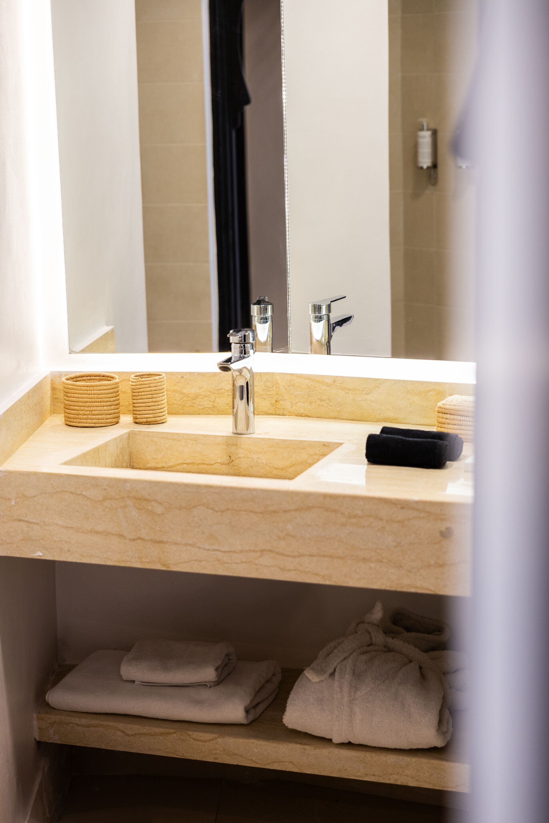 A bathroom with a marble sink, a mirror, and a shelf with folded towels.