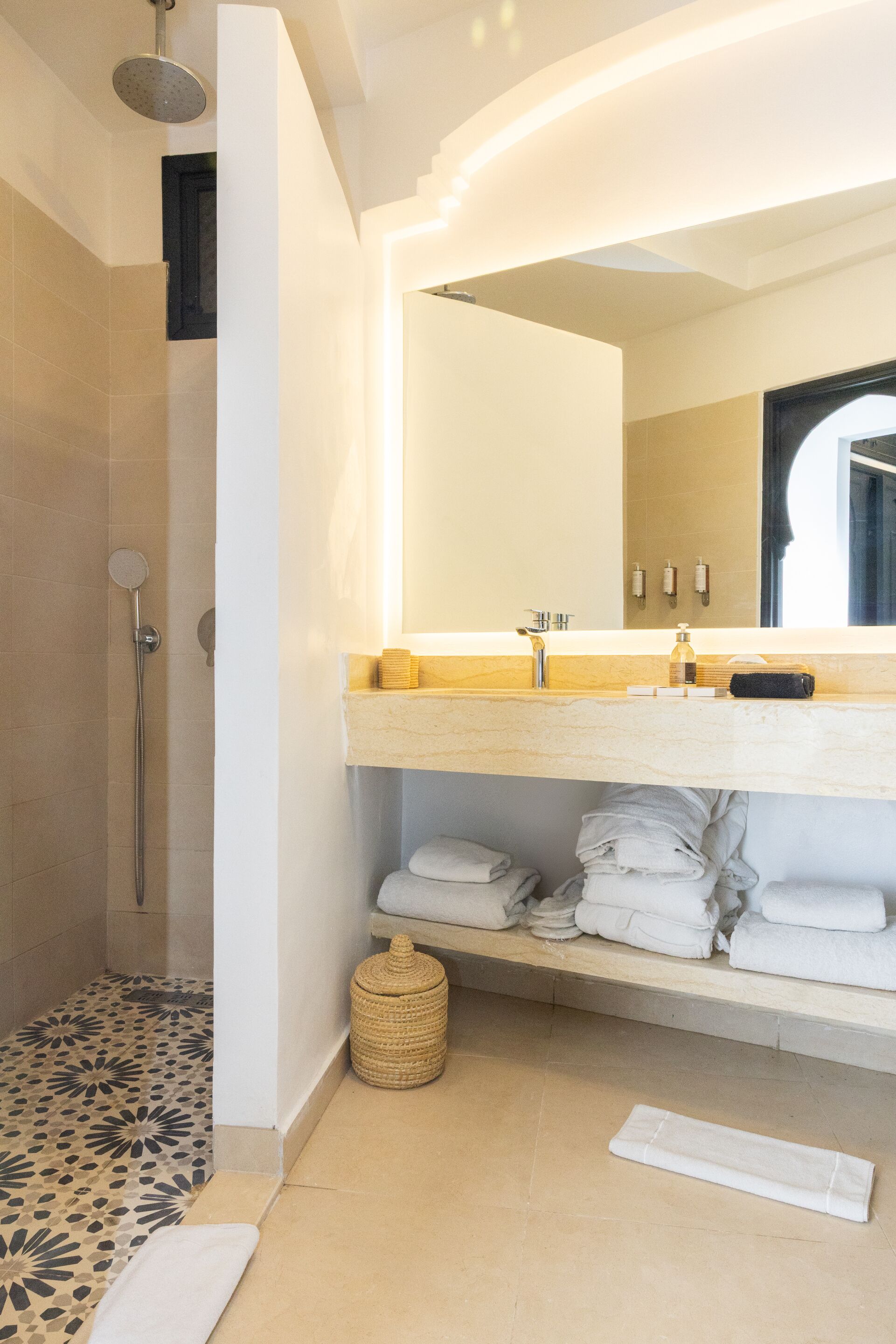 Un baño moderno con ducha, un lavabo con espejo y toallas ordenadas en un estante.