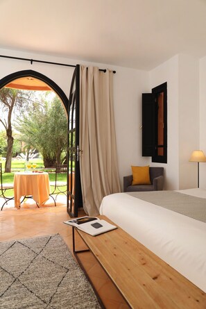 Una habitación con cama, una mesa, una silla, una lámpara y una puerta abierta que da a un balcón con mesa y sillas.
