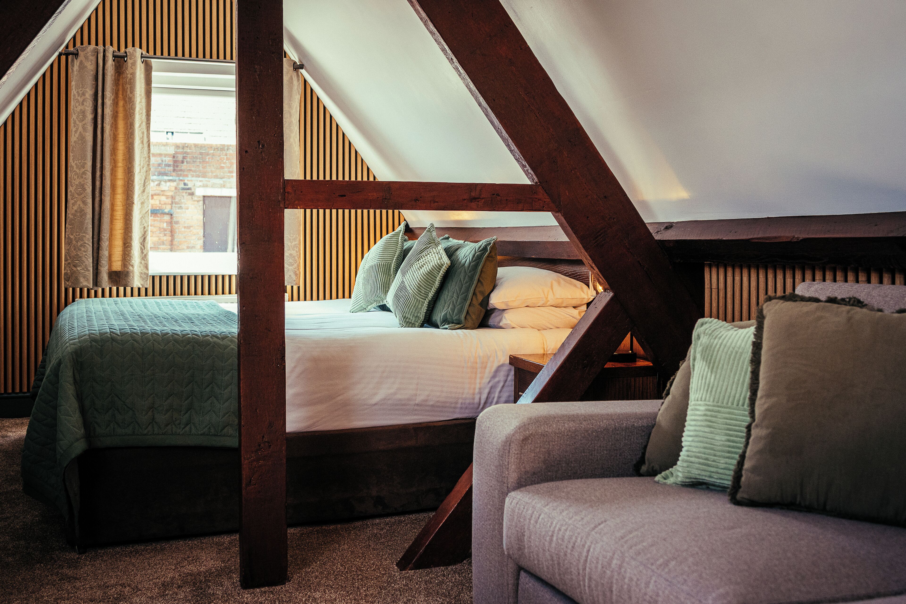 A loft-style bedroom with a sloped ceiling, a bed with pillows, a couch, and wooden paneling.
