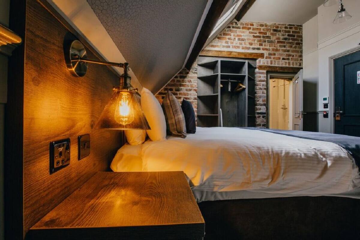 A cozy bedroom with a wooden headboard, a bedside lamp, a brick wall, and a built-in shelving unit.