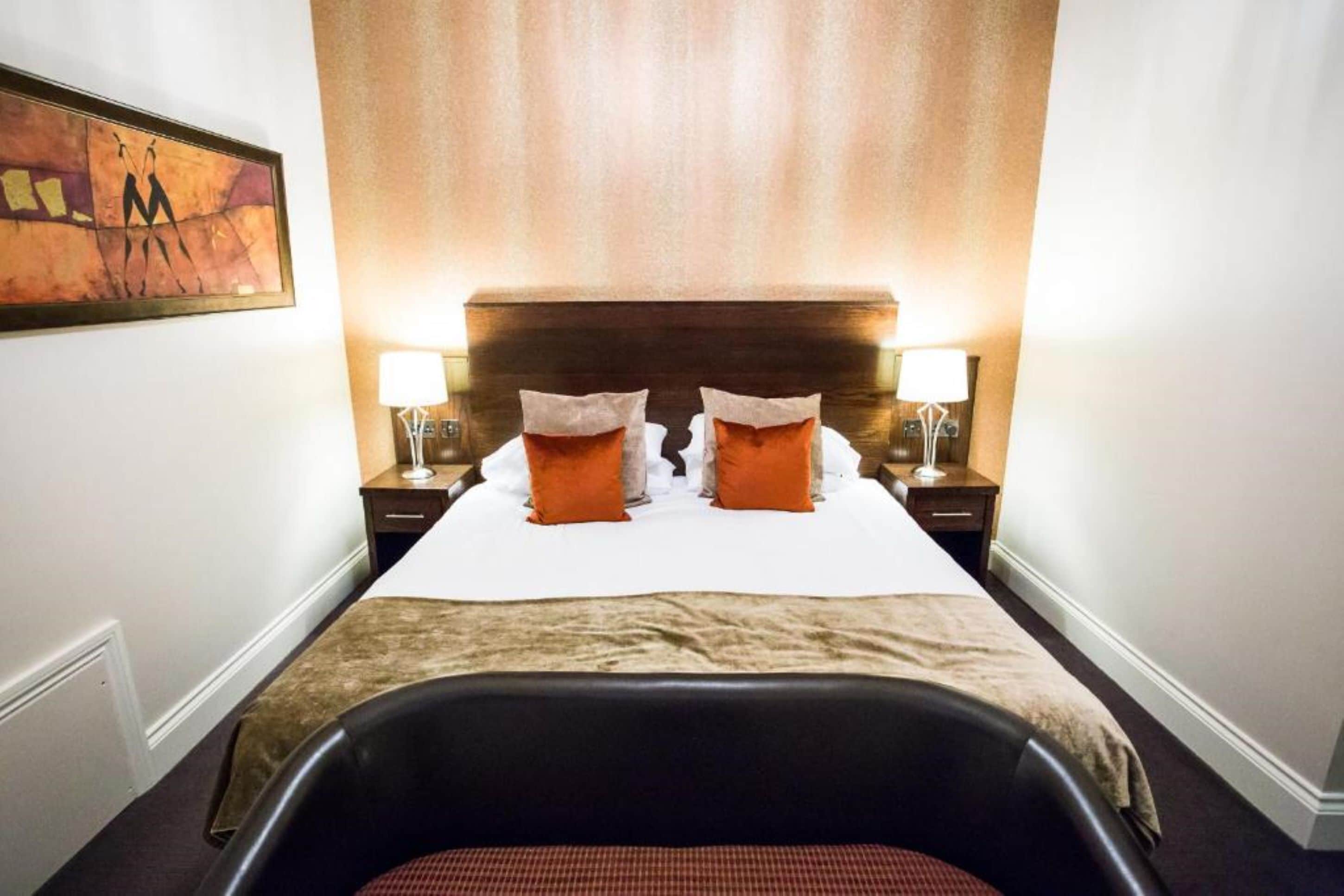 A hotel room with a large bed, two bedside lamps, a headboard, and a painting on the wall.