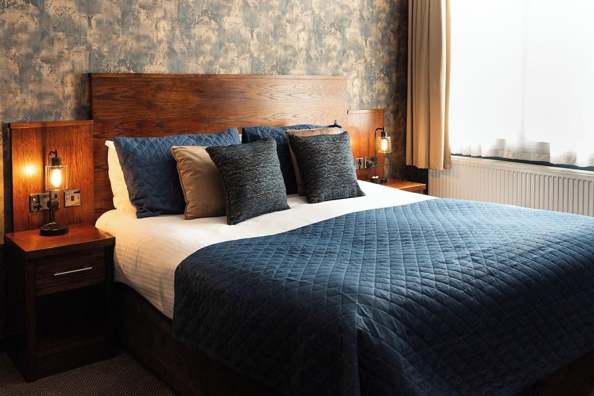 A neatly made bed with a dark blue quilt and multiple pillows, a wooden headboard, and two bedside lamps on wooden nightstands.