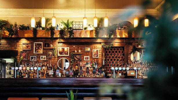 A bar area with a brick wall, shelves of bottles, and hanging lights. - Duke Of Edinburgh Hotel (Barrow-in-Furness)