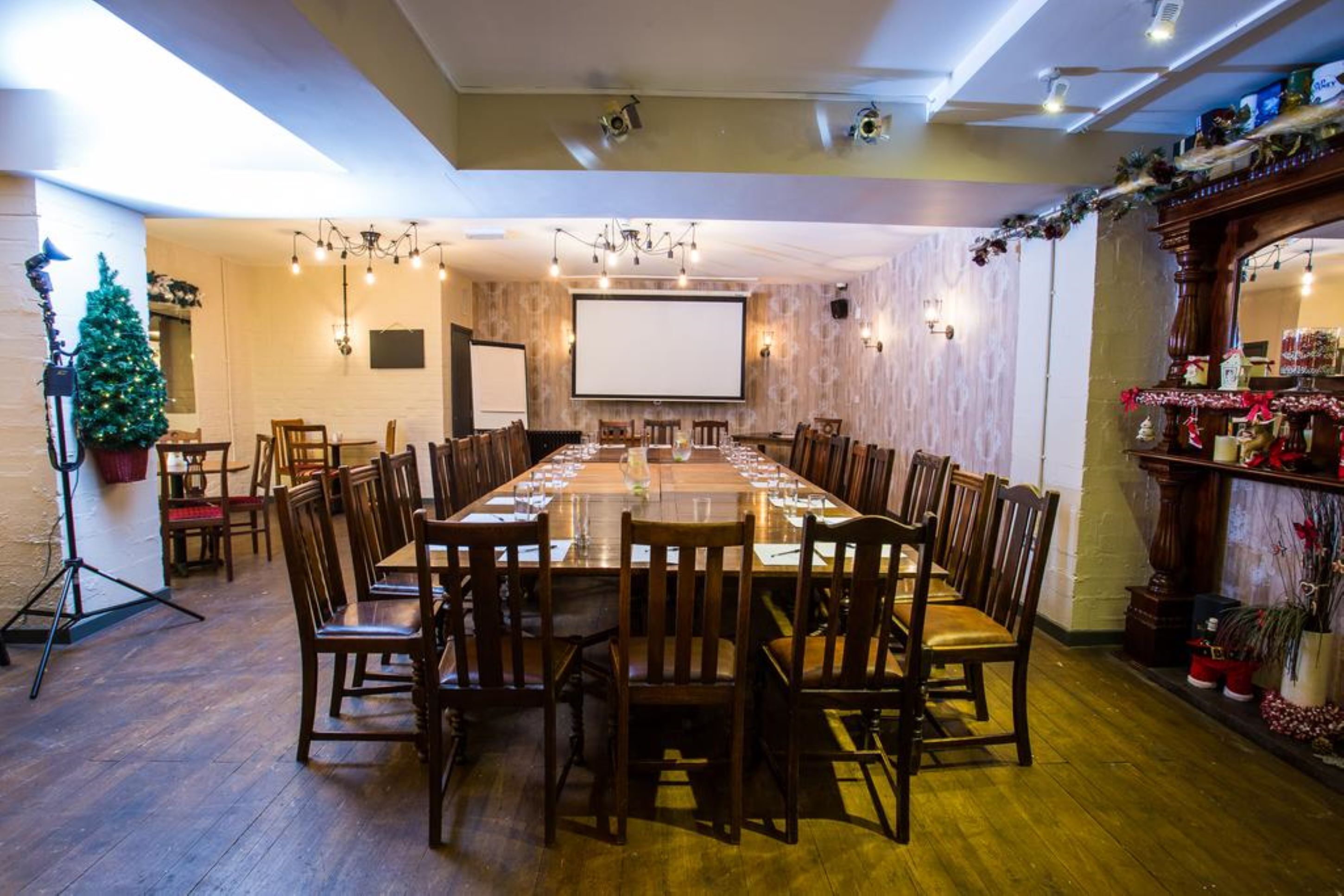 A conference room with a long table, chairs, a projector screen, and a Christmas tree.
