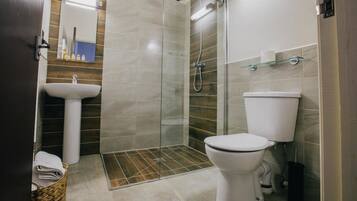 Un baño moderno con ducha de vidrio, lavamanos blanco y retrete.