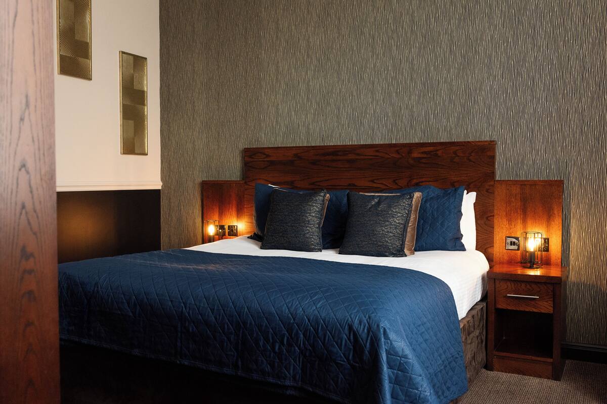 A neatly made bed with a dark blue quilt, two bedside lamps, and a wooden headboard.