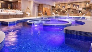Un área de piscina interior lujosa con múltiples jacuzzis y un espacio de estar con sofá y sillones.