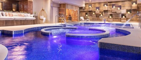 Un área de piscina interior lujosa con múltiples jacuzzis y un espacio de estar con sofá y sillones.