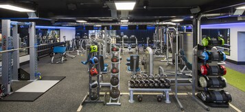 Un gimnasio con diversos equipos de ejercicio, que incluyen máquinas de pesas, pesas libres y máquinas de cardio.