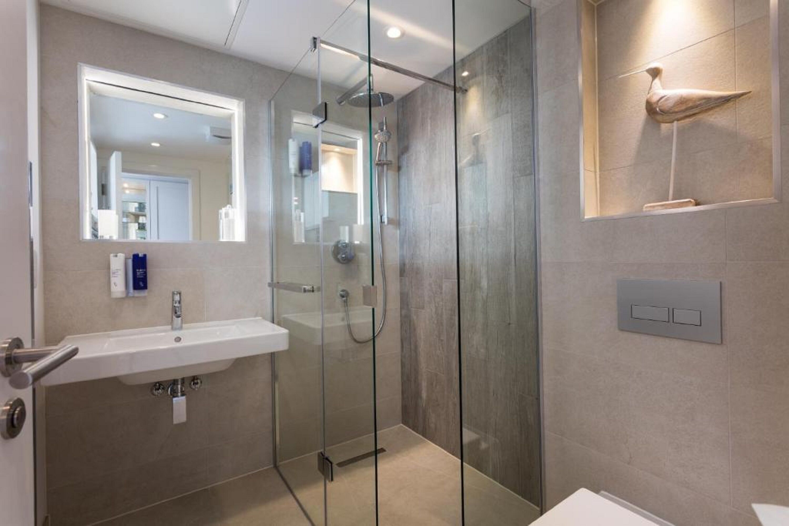 Un baño moderno con cabina de ducha de vidrio, un lavamanos blanco y un espejo.