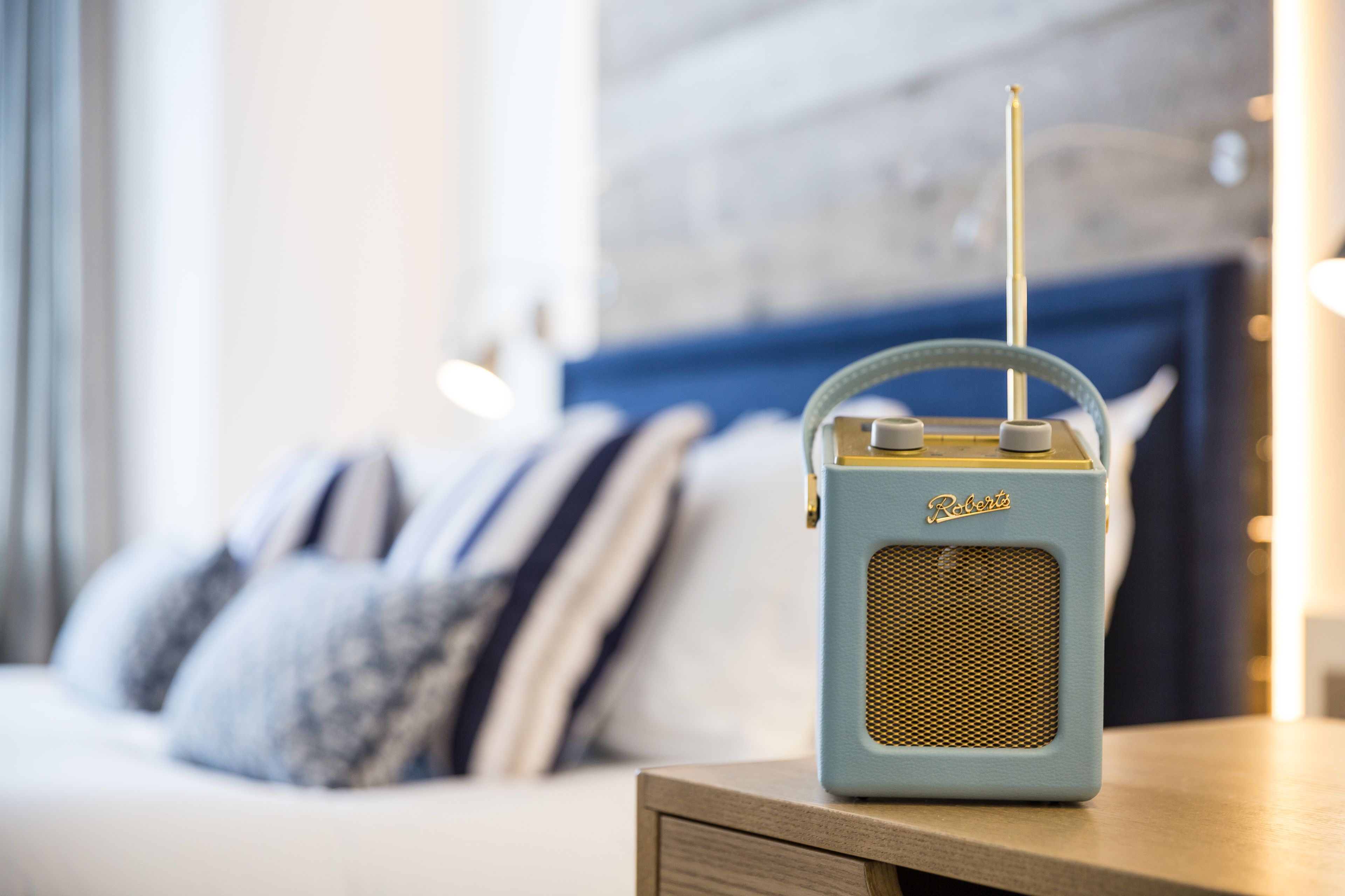 A vintage radio on a bedside table in a modern bedroom with a blue headboard and striped pillows.