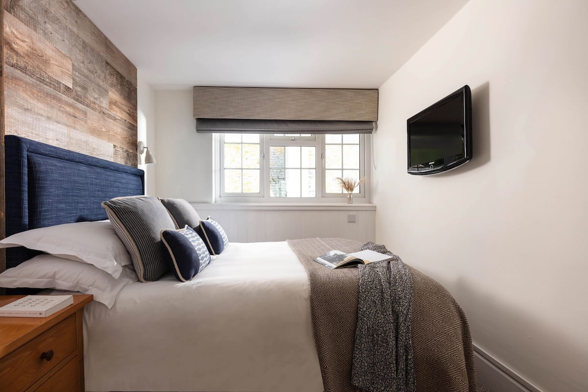 A neatly made bed with a blue headboard, a bedside table with a book, and a wall-mounted TV.