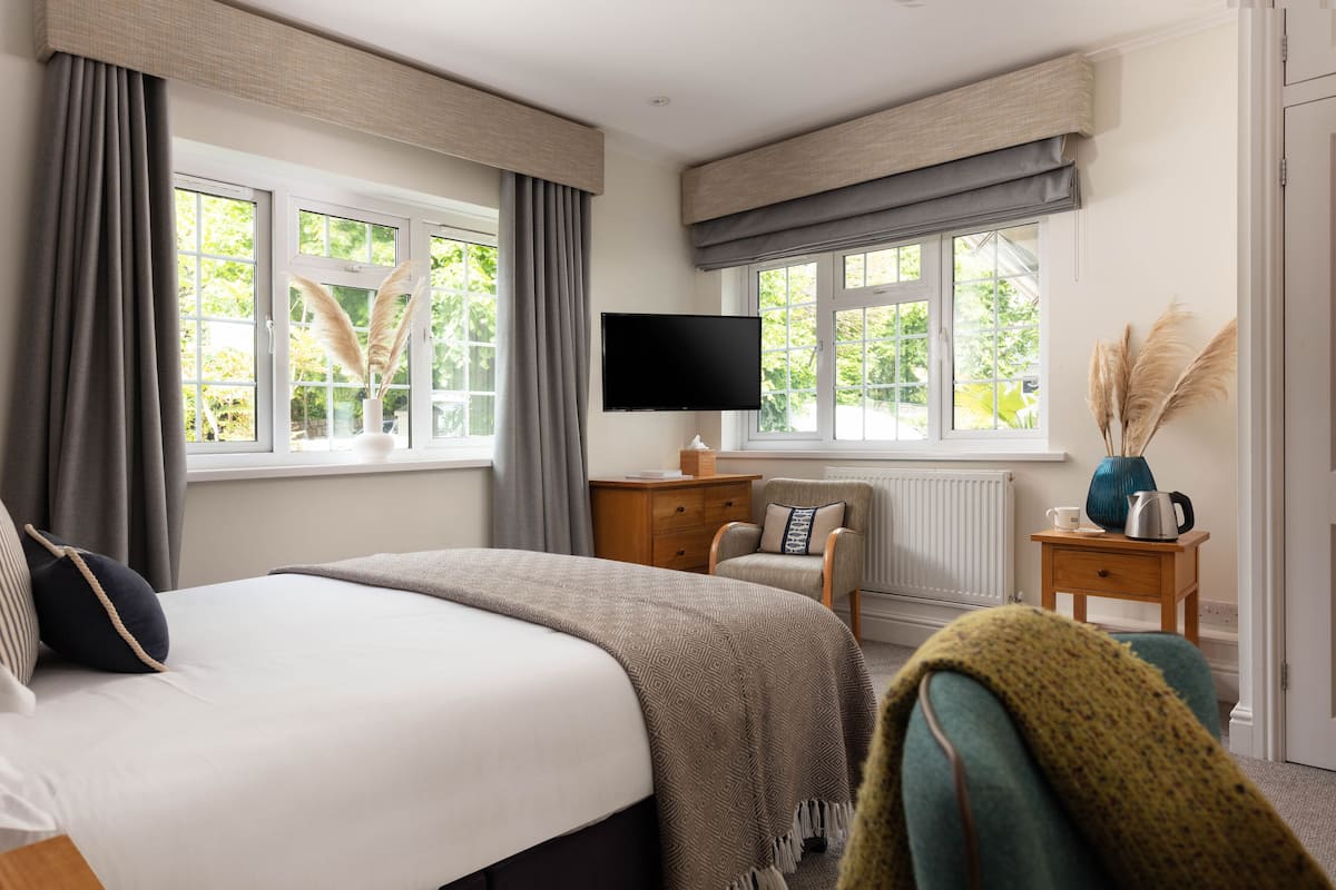 A hotel room with a bed, a chair, a TV, and a window with curtains.