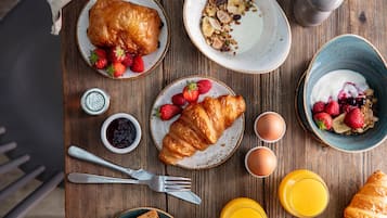 A wooden table with breakfast items including croissants, strawberries, yogurt, and orange juice.