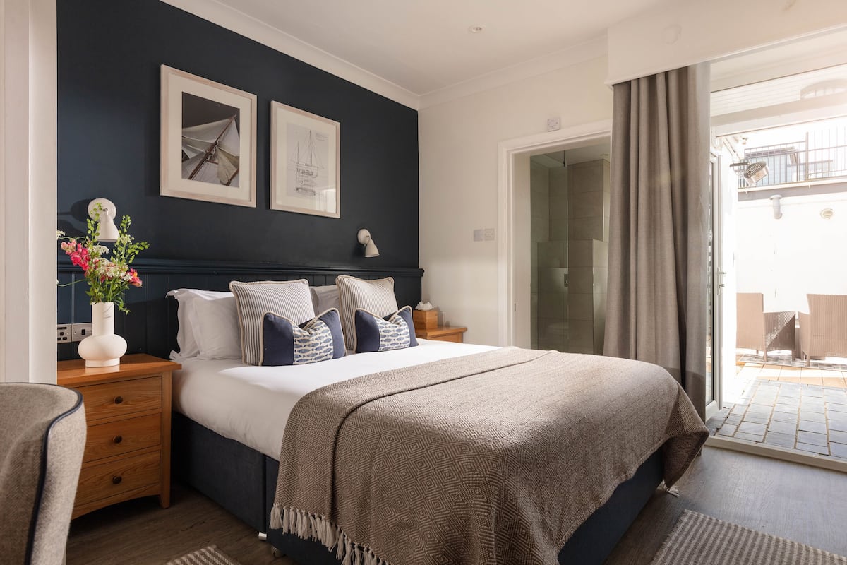 A bedroom with a bed, bedside tables, a nightstand, a vase with flowers, and a view of the outside balcony.
