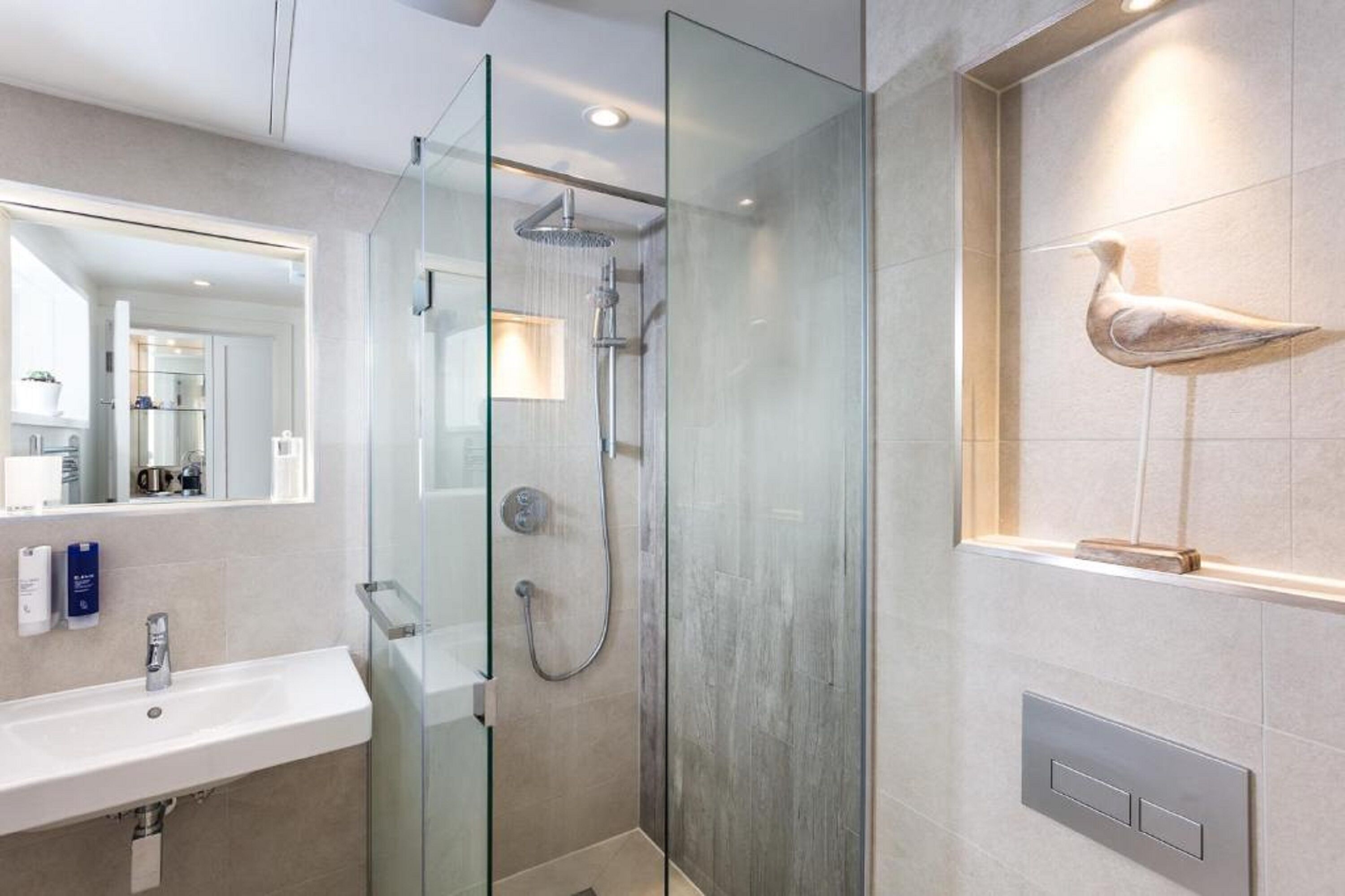 A modern bathroom with a glass-enclosed shower, a large mirror, and a wall-mounted light fixture.