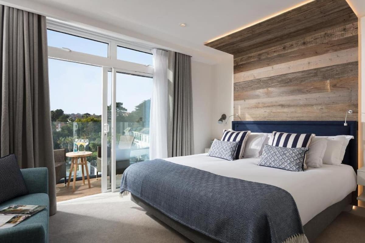 A modern bedroom with a large bed, a wooden accent wall, and a balcony with a view.