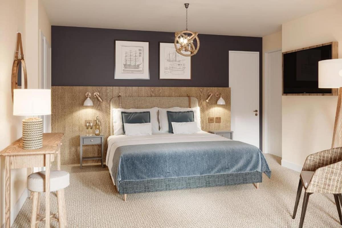 A modern bedroom with a large bed, bedside lamps, a wooden headboard, and artwork on the wall.