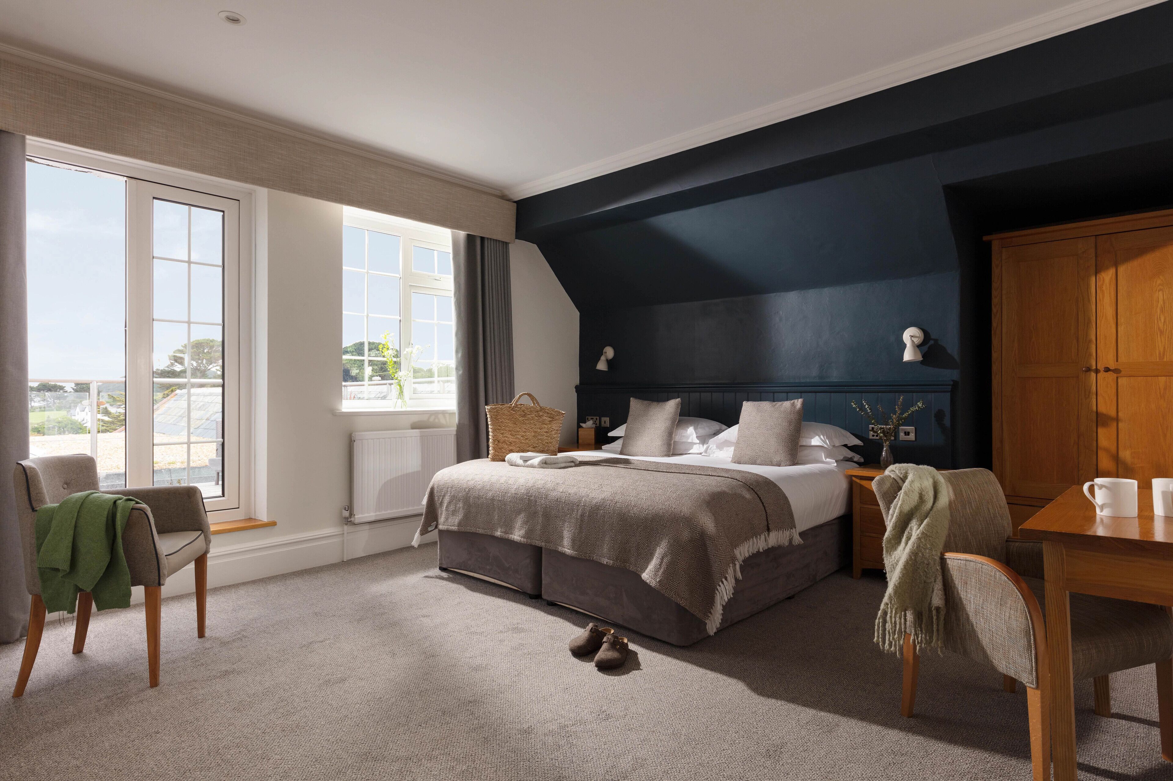 Un dormitorio con una cama grande, una mesita de noche de madera, una silla, una mesa y vistas al exterior.