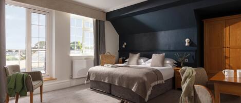 Un dormitorio con una cama grande, una mesita de noche de madera, una silla, una mesa y vistas al exterior.