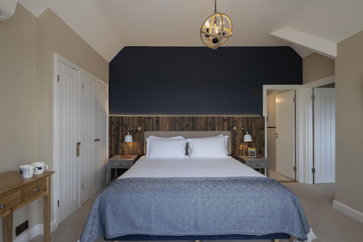 A bedroom with a large bed, two bedside tables with lamps, a wooden headboard, and a hanging light fixture.