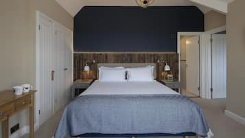 Quarto com uma cama grande, duas mesas de cabeceira com abajures, uma cabeceira de madeira e um lustre.
