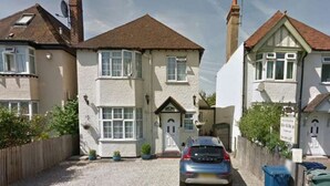 A two-story house with a gravel driveway and a parked car.