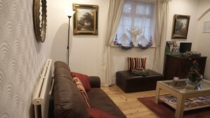 A living room with a brown sofa, a glass coffee table, a black ottoman, and a window with curtains.
