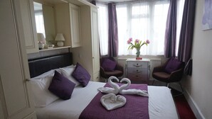 A hotel room with a bed, a nightstand, a chair, a dresser, and a window with curtains.