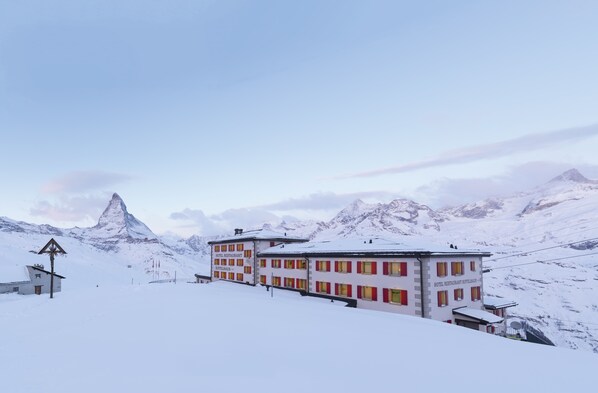 A hotel building with a sign reading "HOTEL RESTAURANT REIFELBACHUS" in a snowy mountainous area.