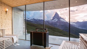 Un interior moderno con ventanas amplias que ofrecen vista a la montaña, mobiliario de madera y un área de sauna.