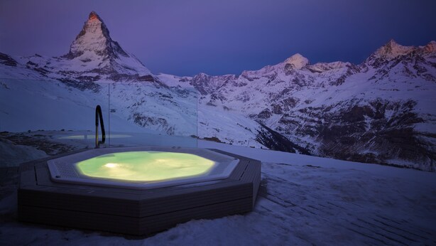 Un jacuzzi en una montaña nevada con vistas a un pico montañoso.