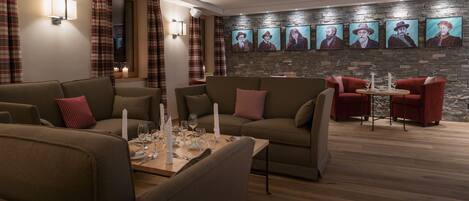 A modern living room with sofas, a dining table set for four, and a stone wall with portraits.