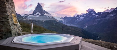 A hot tub on a wooden deck with a mountain view.