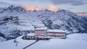 Un hotel con una imponente montaña nevada al fondo, que cuenta con un edificio grande con múltiples ventanas y una entrada central.