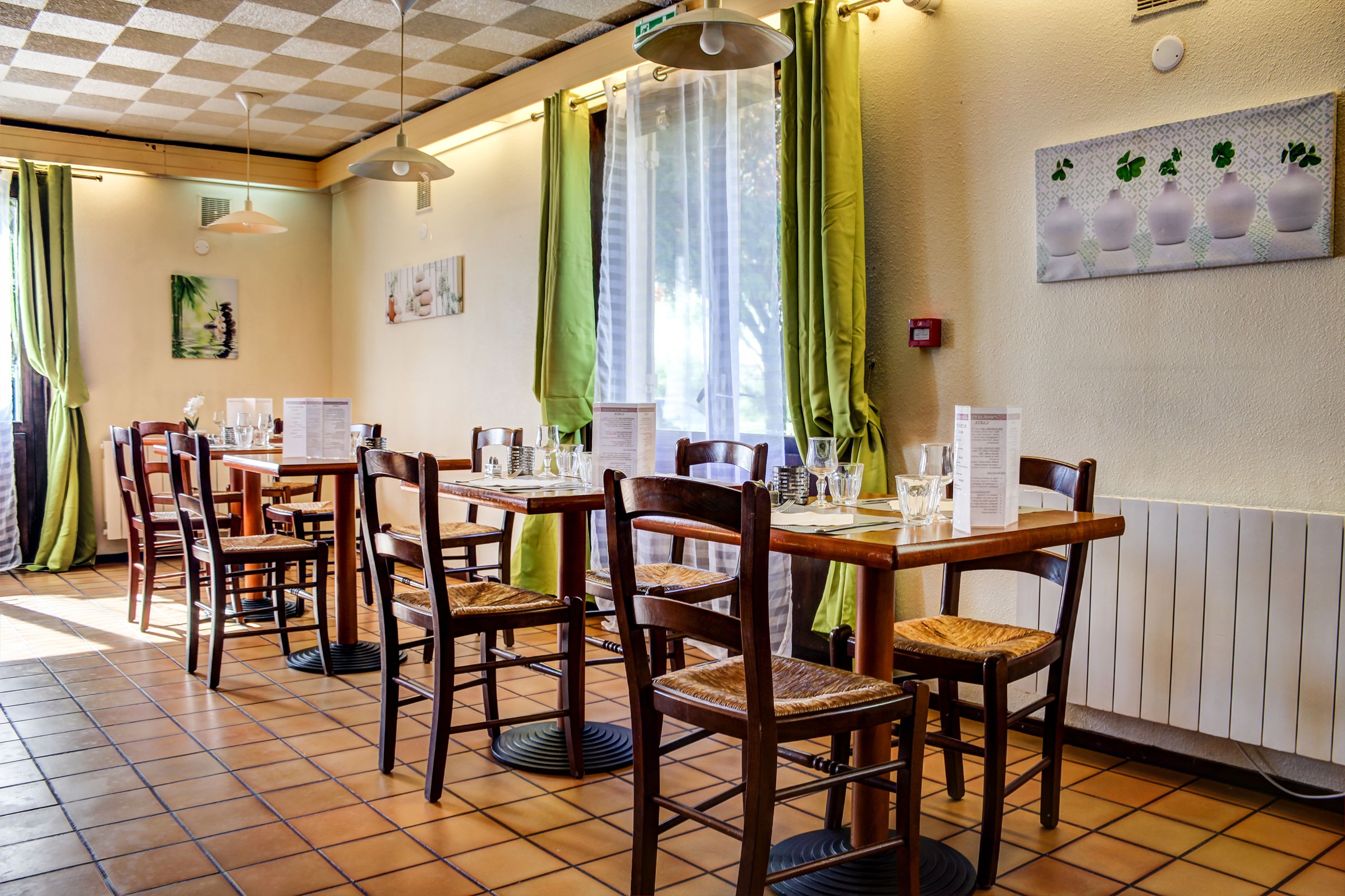 A dining area with wooden tables and chairs, green curtains, and a wall-mounted menu board.