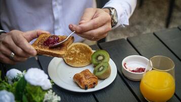 A breakfast setting with toast, pancakes, kiwi slices, croissant, and orange juice on a table.