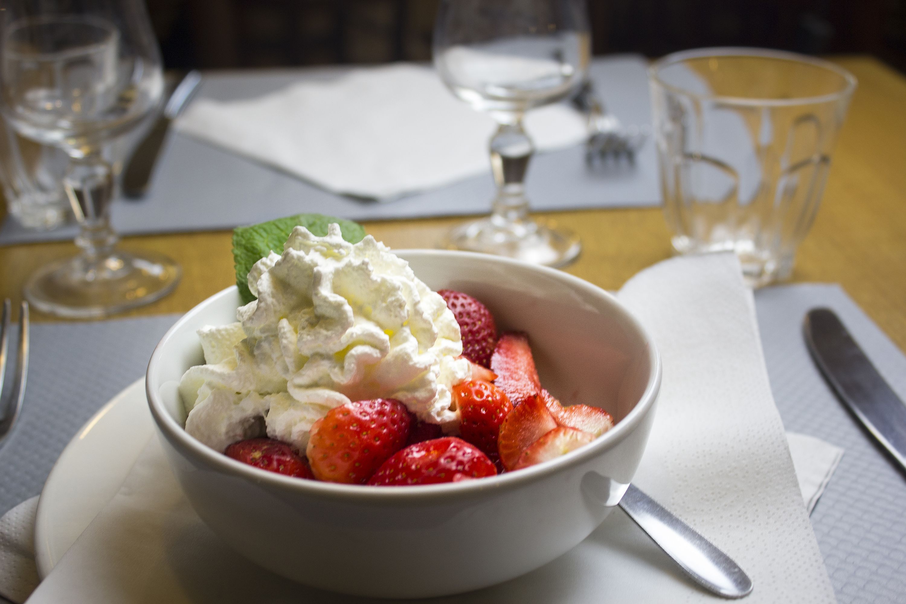 Un tazón de fresas y crema batida sobre un plato blanco.