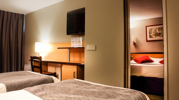 Een hotelkamer met twee bedden, een bureau, een stoel, een televisie en een deur naar een andere kamer.