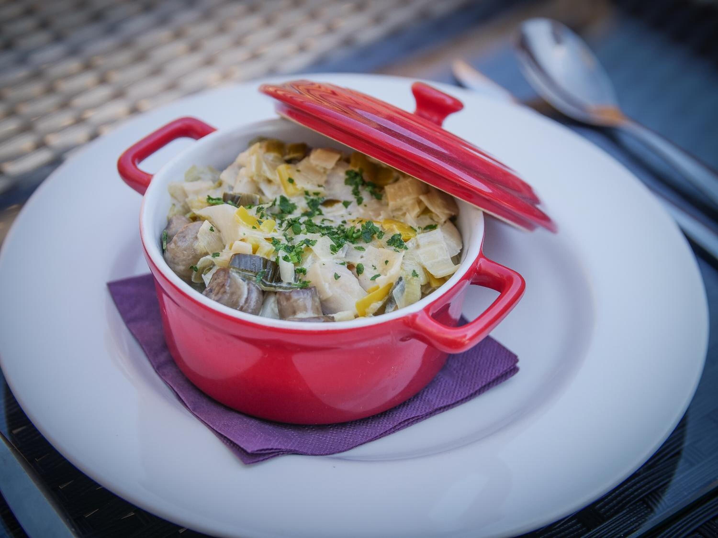 A red pot of food on a white plate with a purple napkin underneath.