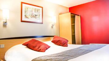 Habitación de hotel con una cama, dos almohadas rojas, un armario de madera y un cuadro enmarcado en la pared.